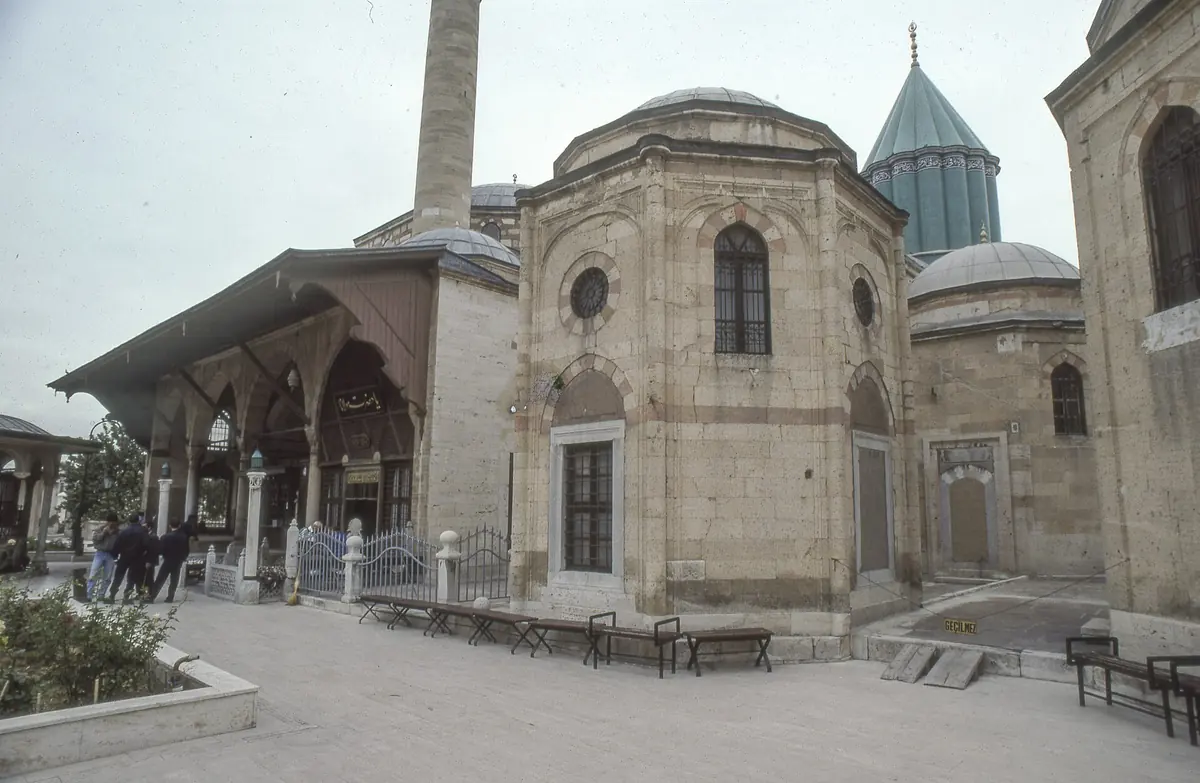 The Mevlâna Museum in Konya, with a stone mausoleum and a turquoise-tiled dome behind an open arcade.